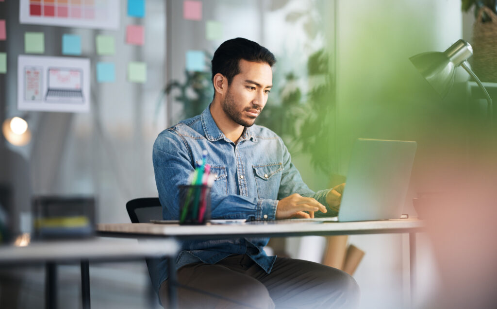 Thinking, typing and man at desk with laptop, ideas and research planning at design agency. Business, work and computer, employee in office reading email or online report in creative startup career.
