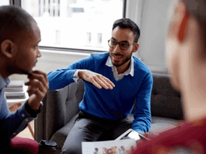 Man in blue jumper and glasses chats to a colleague