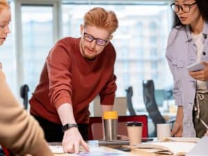 Confident young businessman pointing at financial paper while showing and explaining his colleagues some important information
